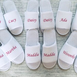 May include: White slippers with pink embroidered names, including Lucy, Daisy, Ada, Martha, Maddie, and Weronika.