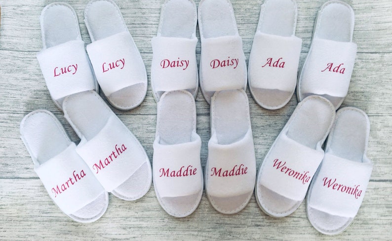 May include: White slippers with pink embroidered names, including Lucy, Daisy, Ada, Martha, Maddie, and Weronika.