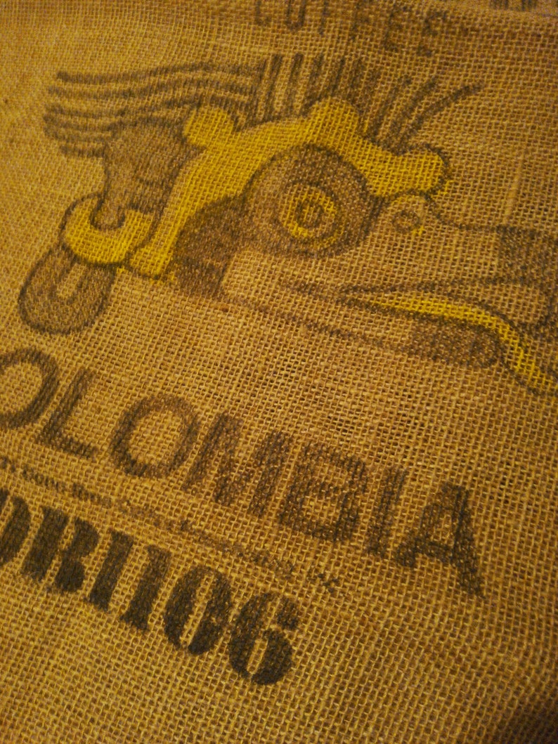 May include: A brown burlap sack with a yellow and black printed design of a flying bird. The text "Colombia" and "Orions" is printed on the sack.