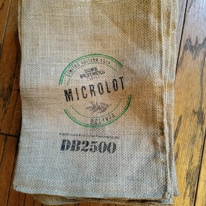 Puede incluir: Un montón de sacos de arpillera marrones con una etiqueta verde y negra que dice "Limited Edition 2023 Dunn Brothers Coffee Microlot Bolivia" y un número negro "DL25009".