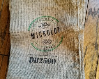 May include: A stack of brown burlap sacks with a green and black label that reads "Limited Edition 2023 Dunn Brothers Coffee Microlot Bolivia" and a black number "DL25009".