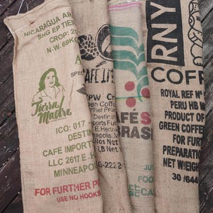 May include: Four rectangular burlap coffee sacks with various printed graphics and text. The sacks feature labels including Tierra Madre, Cafe Imports, and Peru HB. The text includes details like Nicaragua, Crop 20, and Net Weight 69KG, with visible red and green ink.