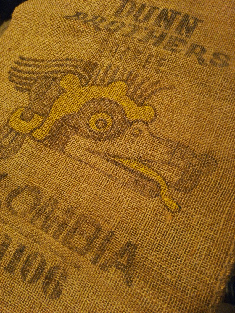 May include: A brown burlap sack with a yellow and black eagle design and the text "MINN.  CO-OP.  CREAMERIES" printed on the surface.