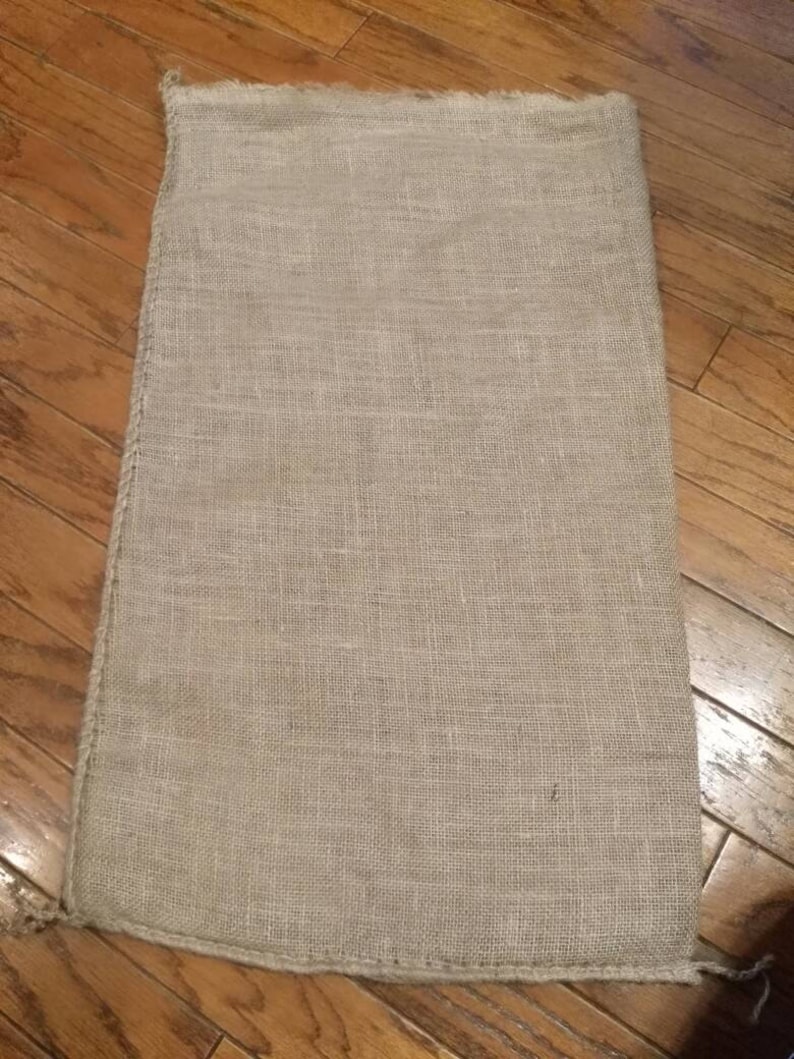 May include: A large, natural burlap sack with a rough, woven texture. The sack is empty and has a frayed edge.