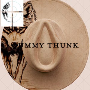 May include: Tan fedora hat with a detailed wolf illustration on the side. The hat features the text "UMMY THUNK" in black. The hat has a structured crown and a wide brim, suitable for sun protection.
