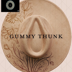 May include: A beige fedora hat with a wide brim, featuring a floral design in brown tones. The hat has the text "GUMMY THUNK" in black across the crown. A small circular graphic is in the upper left corner.