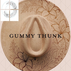May include: A tan fedora-style hat with a wide brim, featuring a floral design in brown. The hat has the text "GUMMY THUNK" in black across the front. The floral pattern includes lilies and leaves.