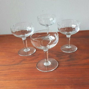 May include: Four clear glass stemmed drinking glasses with etched designs on a wooden table.
