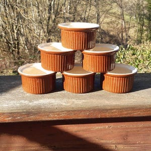 Puede incluir: Un juego de seis ramequines de cerámica marrón con interiores blancos. Los ramequines están apilados en forma de pirámide.