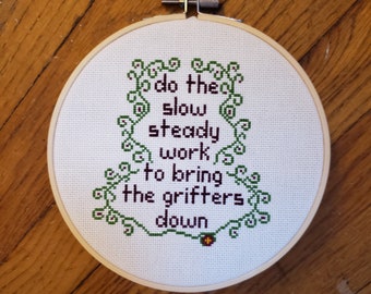 Do the Slow Steady Work to Bring the Grifters Down, completed cross stitch, framed in 6 inch hoop