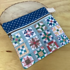 May include: A rectangular zippered pouch featuring a patchwork quilt design with various geometric star and square patterns in shades of blue, green, red, and yellow. The top section is a solid dark blue fabric with a small white floral print.