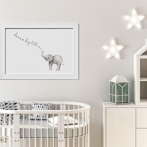 May include: A white framed print with a watercolor illustration of a grey elephant with the text "dream big little one" above it. The print is hanging on a white wall with two white star-shaped lights above it.
