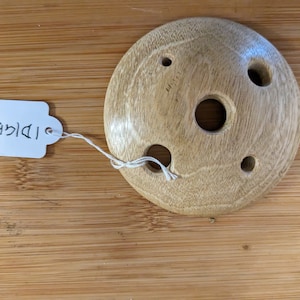 以下が含まれることがあります： 5つの穴が開けられた木製の円盤。円盤は薄い茶色で、滑らかで磨かれた仕上げになっています。円盤に付けられたタグには「ID158C」と書いてあります。