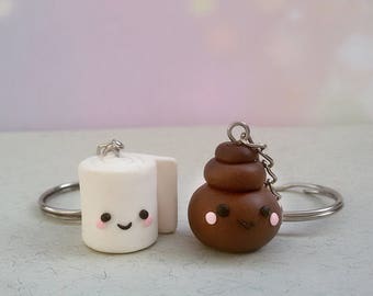 Puede incluir: Un par de llaveros con un rollo de papel higiénico blanco y un emoji de caca marrón, ambos con caras de dibujos animados lindas. Los llaveros están hechos de arcilla polimérica y tienen llaveros de metal plateado.