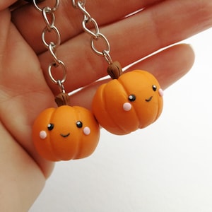 May include: Two orange pumpkin charms with happy faces and pink cheeks, attached to silver chains.