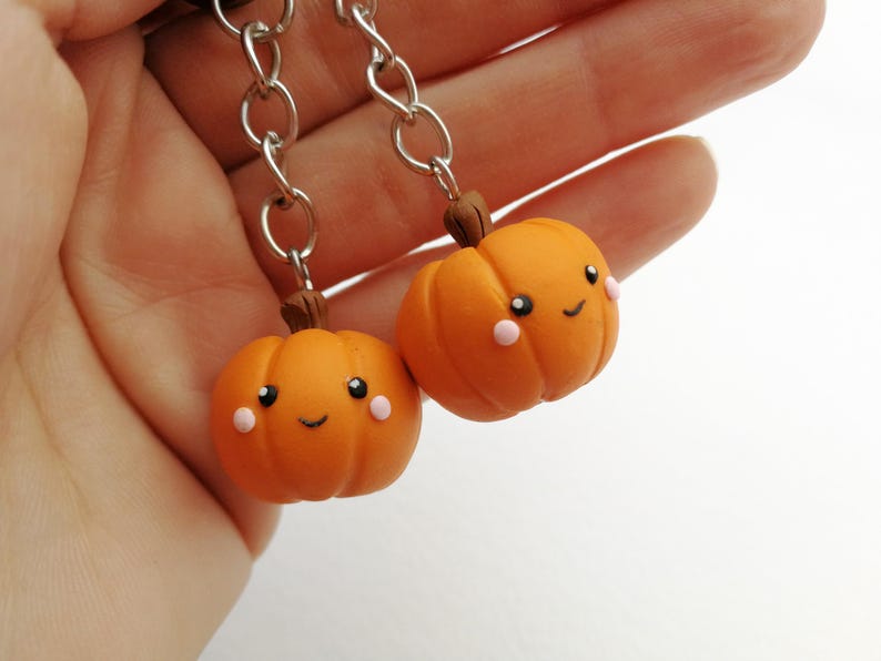 May include: Two orange pumpkin charms with happy faces and pink cheeks, attached to silver chains.