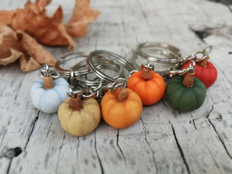 Puede incluir: Un conjunto de seis llaveros de calabaza de colores. Los llaveros est&aacute;n hechos de arcilla polim&eacute;rica y presentan diferentes tonos de naranja, verde, azul y amarillo. Cada calabaza tiene un peque&ntilde;o tallo y est&aacute; unida a un llavero plateado.