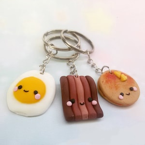 Puede incluir: Tres llaveros lindos con forma de huevo frito, tocino y panqueque. Cada llavero tiene una carita feliz y est&aacute; unido a un llavero plateado.