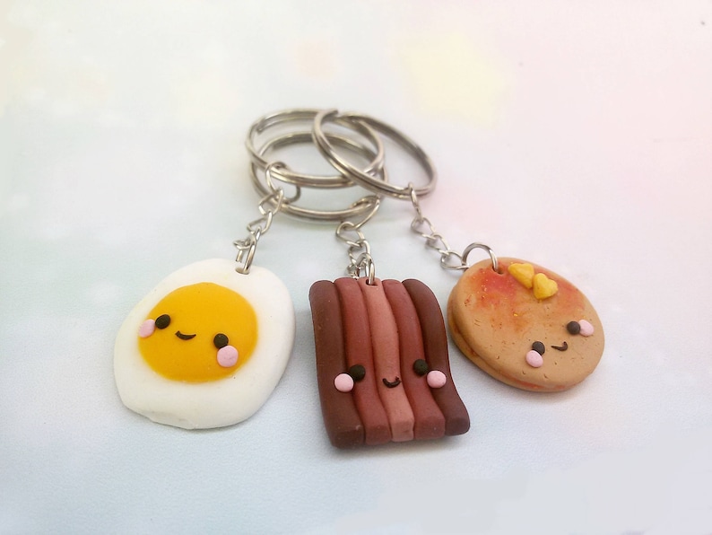 Puede incluir: Tres llaveros lindos con forma de huevo frito, tocino y panqueque. Cada llavero tiene una carita feliz y est&aacute; unido a un llavero plateado.