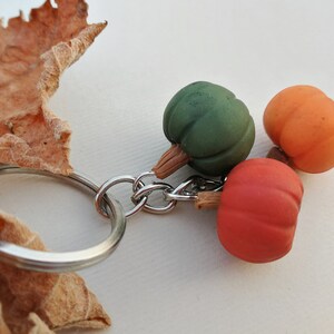 Puede incluir: Un llavero de plata con tres peque&ntilde;os abalorios de calabaza. Las calabazas son verdes, naranjas y rojas.