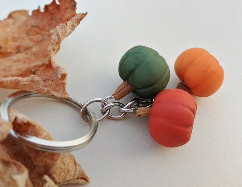 Puede incluir: Un llavero de plata con tres peque&ntilde;os abalorios de calabaza. Las calabazas son verdes, naranjas y rojas.