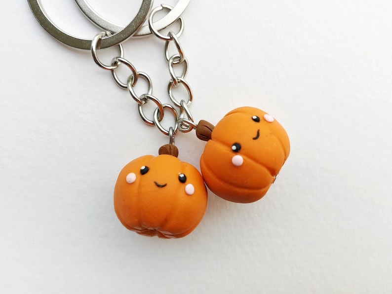 May include: Two orange pumpkin-shaped keychains with happy faces. The keychains are attached to a silver chain.