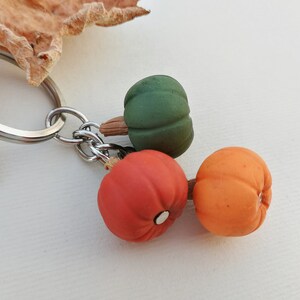 Puede incluir: Un llavero de plata con tres peque&ntilde;as calabazas decorativas. Una calabaza es verde, una es naranja y una es roja.