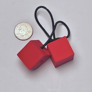 May include: Two red foam dice connected by a black elastic band. The dice are about 2 inches in size.