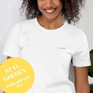 White short sleeve tee with the phrase Stay Golden embroidered in gold thread.