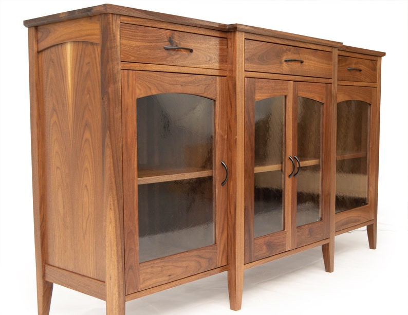 May include: A wooden cabinet with three glass doors and three drawers. The cabinet is made of walnut wood and has a dark brown finish. The doors have black metal handles.