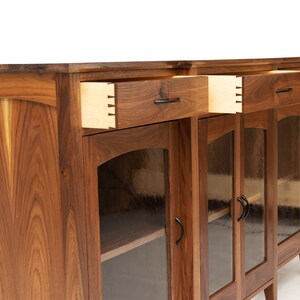 May include: A wooden cabinet with glass doors and drawers. The cabinet is made of walnut wood and has a dark brown finish. The doors have a decorative design and the drawers have black metal handles.