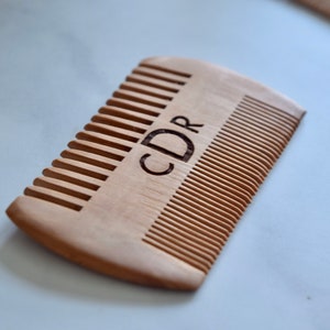 May include: A wooden comb with the initials "CDR" engraved on the handle. The comb has fine teeth and is made of natural wood.
