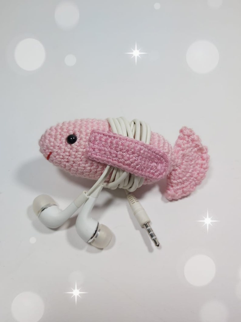 May include: Pink crocheted fish-shaped headphone holder with white cord wrapped around it.