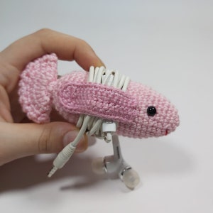 May include: Pink crocheted animal shaped headphone holder with white headphone cords wrapped around it.