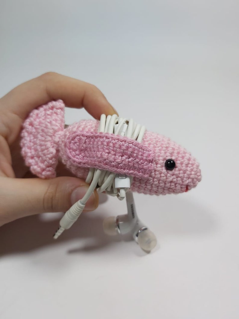 May include: Pink crocheted animal shaped headphone holder with white headphone cords wrapped around it.