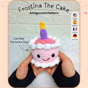 May include: A crocheted pink cake with a smiling face, white frosting, and a purple and yellow candle. The text "Frostina The Cake Amigurumi Pattern" is above the cake. The words "Low Sew" are also visible.