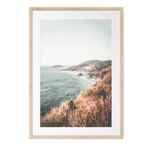 May include: A framed photograph of a coastal landscape with a rocky coastline and blue water. The photo is taken from a high vantage point, looking down at the ocean. The colors are muted and the overall tone is serene.