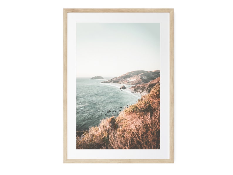 May include: A framed photograph of a coastal landscape with a rocky coastline and blue water. The photo is taken from a high vantage point, looking down at the ocean. The colors are muted and the overall tone is serene.