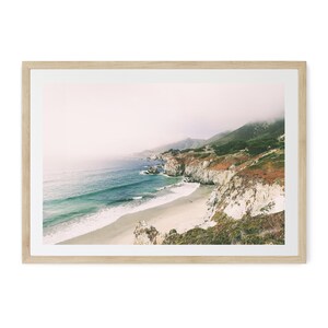 Peut inclure: Impression d'un paysage c&ocirc;tier avec plage, mer et falaises. La photographie est encadr&eacute;e dans un cadre en bois clair. La mer est turquoise et les falaises sont un m&eacute;lange de blanc et de brun. Le ciel est couvert.
