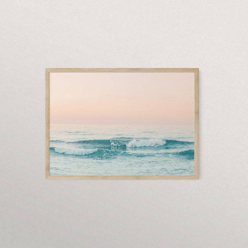 May include: A framed photograph of a seascape with turquoise water and white foamy waves crashing against the shore. The sky is a soft pink color, suggesting a sunset or sunrise.