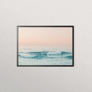 May include: A framed photograph of a seascape with soft, pastel pink and blue hues. The image features a series of waves crashing on the ocean surface, creating a tranquil and serene atmosphere.