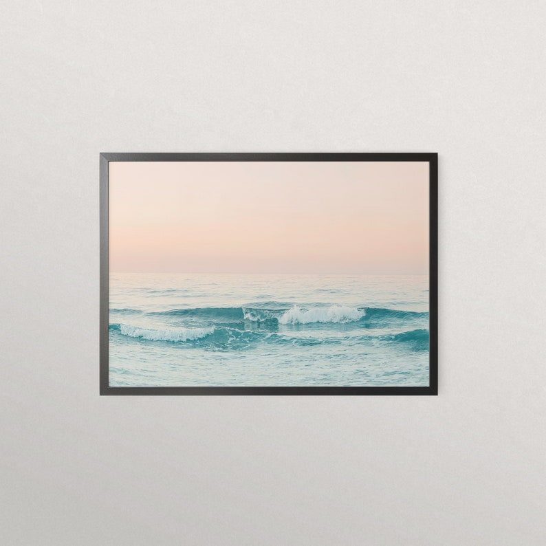 May include: A framed photograph of a seascape with soft, pastel pink and blue hues. The image features a series of waves crashing on the ocean surface, creating a tranquil and serene atmosphere.