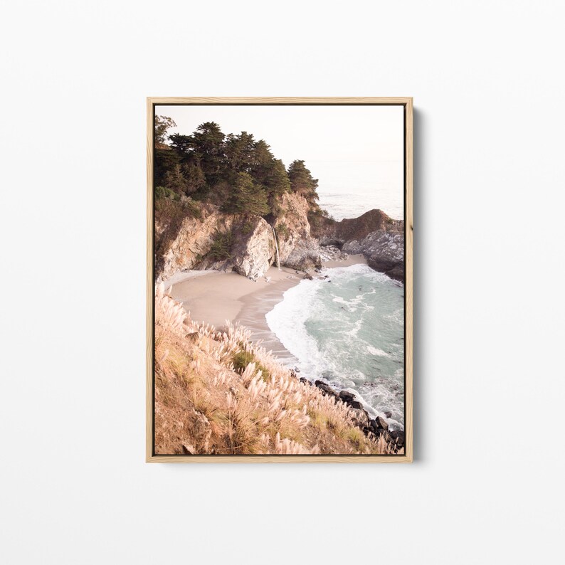 May include: A photograph of a rocky coastline with a small sandy beach and turquoise water. The beach is surrounded by tall cliffs covered in green trees and bushes. The water is crashing against the shore, creating white foam.