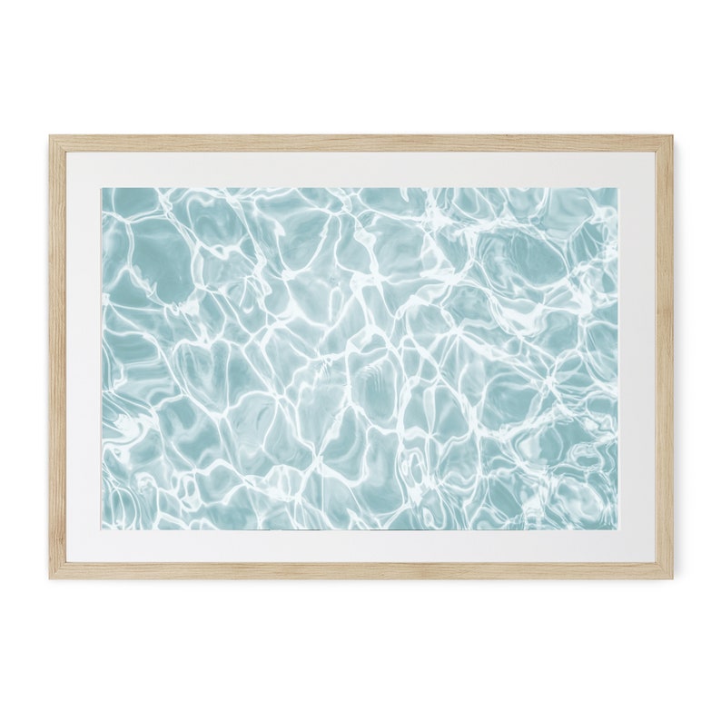 May include: A framed print of an abstract image of rippling water in shades of blue and white.
