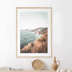 May include: A framed photograph of a coastal landscape with a view of a rocky coastline and the ocean. The photo is in a light wood frame and has a muted color palette.