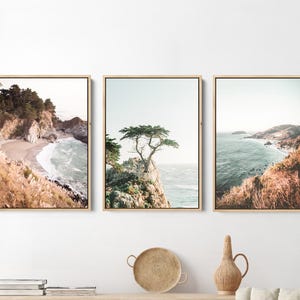 May include: Three framed landscape photographs of a coastal scene with a rocky shoreline, ocean waves, and a lone tree on a cliff. The photos are in a muted color palette with a vintage feel.
