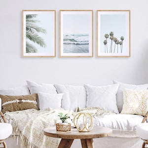 May include: Three framed prints of beach scenes. The left print shows a close-up of palm tree leaves. The center print shows a blue ocean with waves crashing on the shore. The right print shows a row of palm trees against a blue sky.