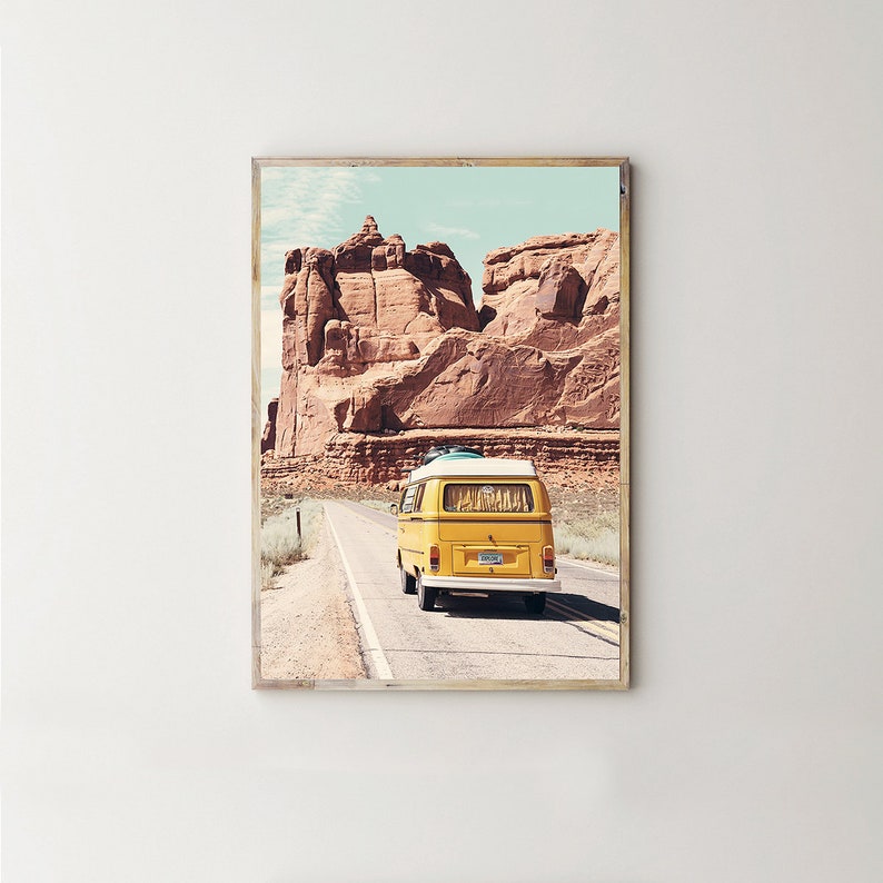 May include: A yellow vintage van drives down a road in a desert landscape with red rock formations in the background.