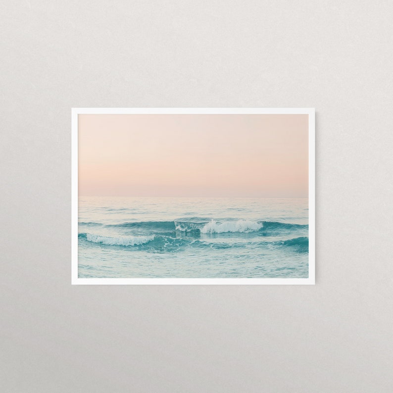 May include: A photograph of a seascape with soft, pink and blue hues. The ocean waves are gently rolling in the foreground, with a light pink sky in the background.