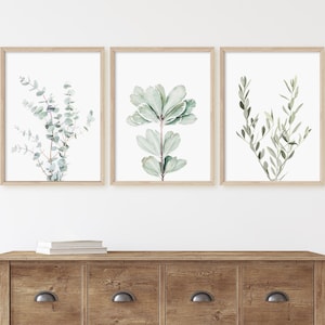 May include: Three framed watercolor prints of green foliage, displayed on a wooden dresser with three drawers.